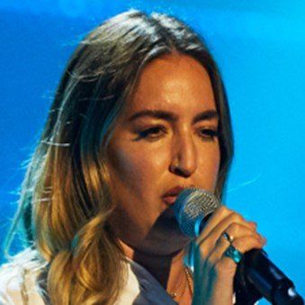 A woman is singing into a microphone with a blue background.