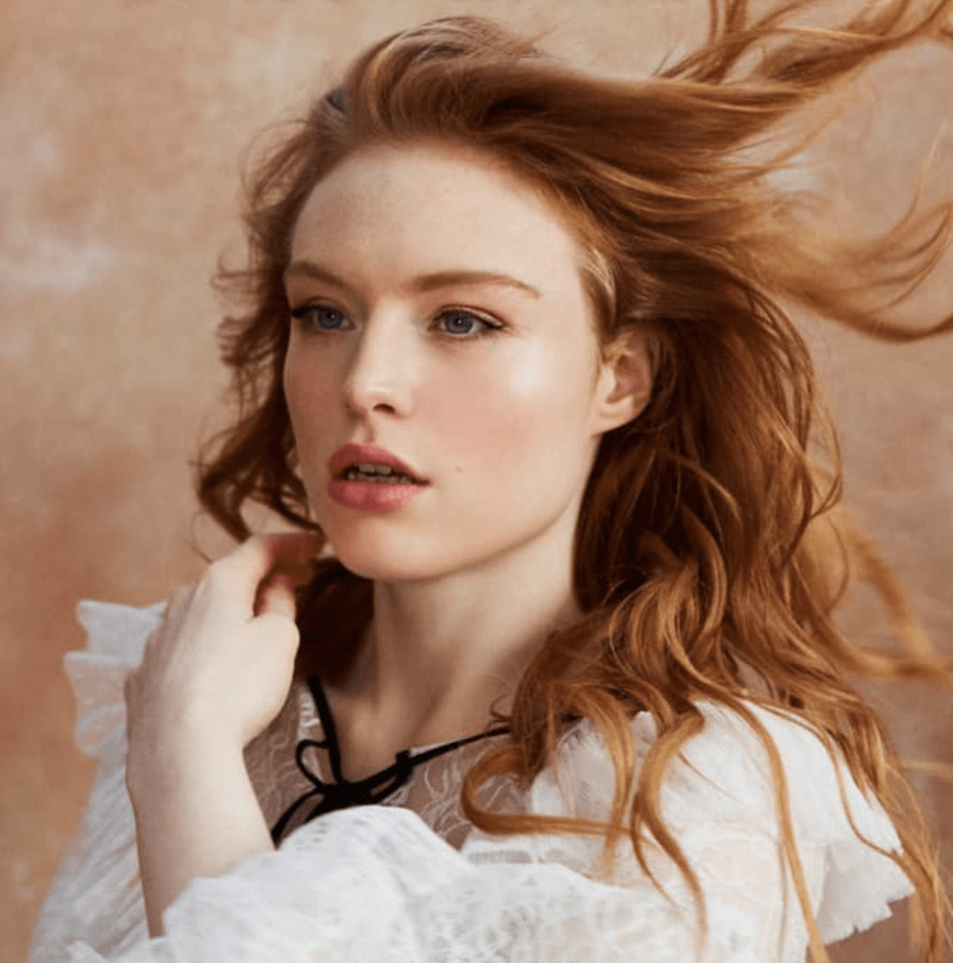 A woman with red hair is wearing a white lace top