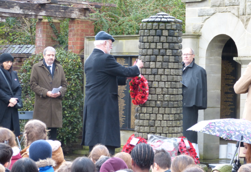 A man is putting a wreath on a brick pillar in front of a crowd of people.