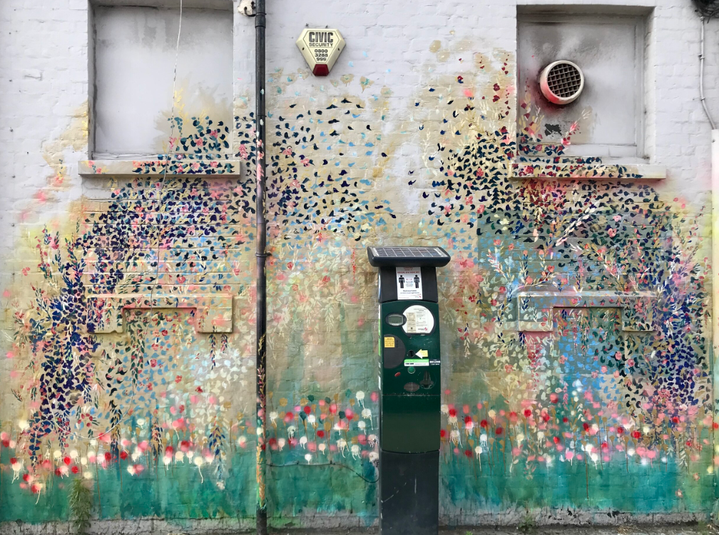 A colorful mural on the side of a building with a parking meter in front of it.