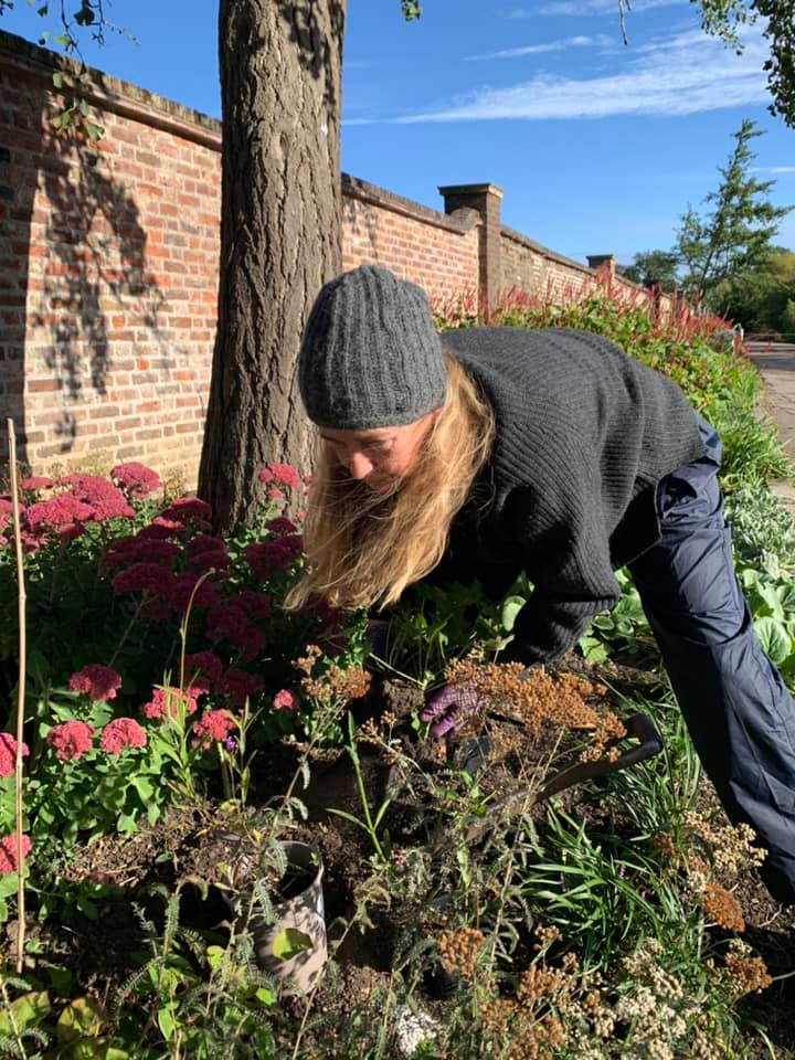A woman is kneeling down in a garden looking at flowers.