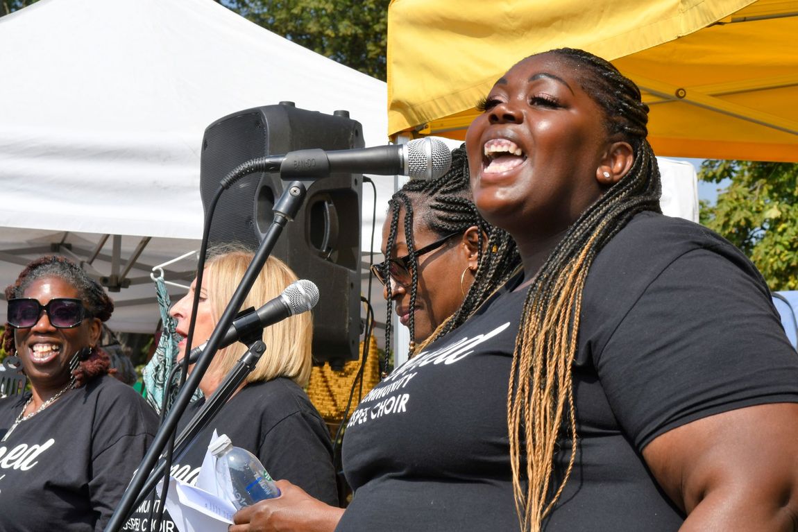 Women singing into microphones at an outdoor event under white and yellow tents