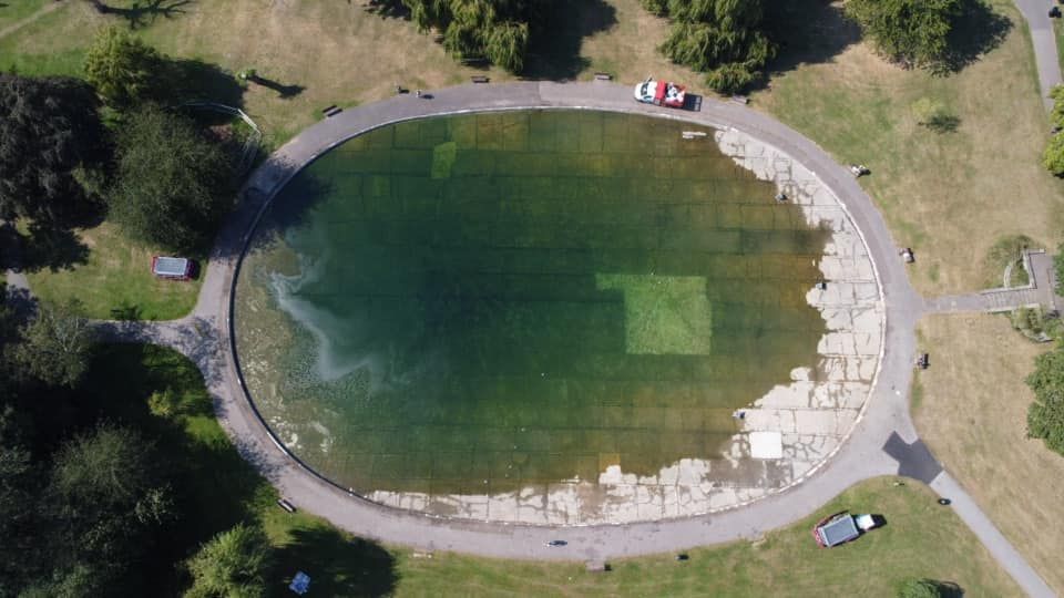 An aerial view of a large oval pond in a park surrounded by trees.
