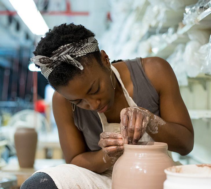 Potter shaping a clay vase on a wheel in a ceramics studio