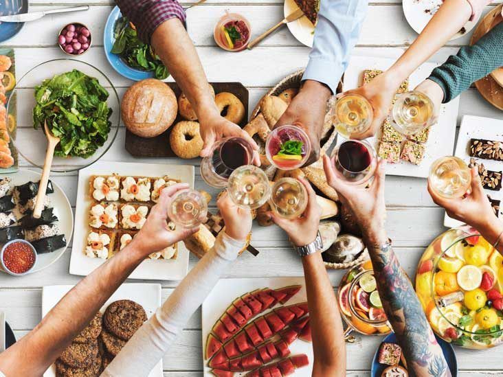 Friends clinking glasses over a colorful shared meal on a bright table