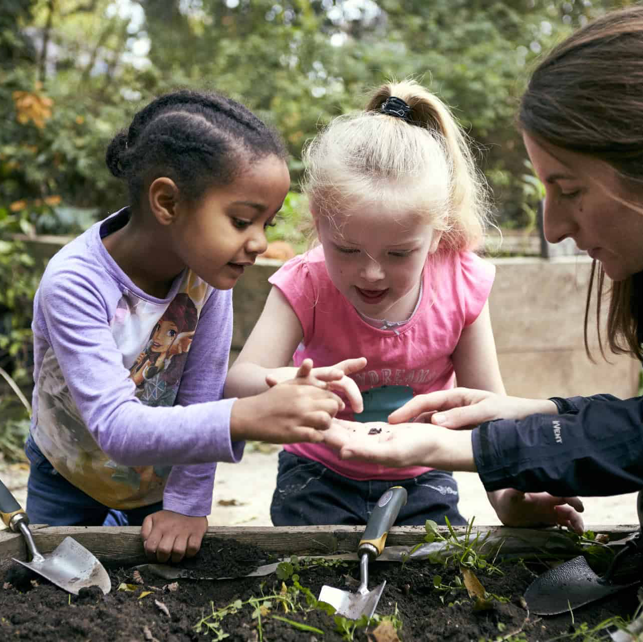 Three little girls are playing with a shovel in the dirt