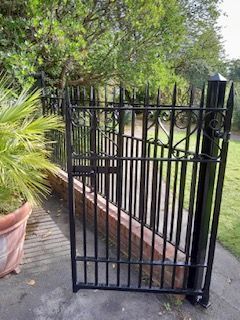 A black gate is sitting next to a fence and a potted plant.