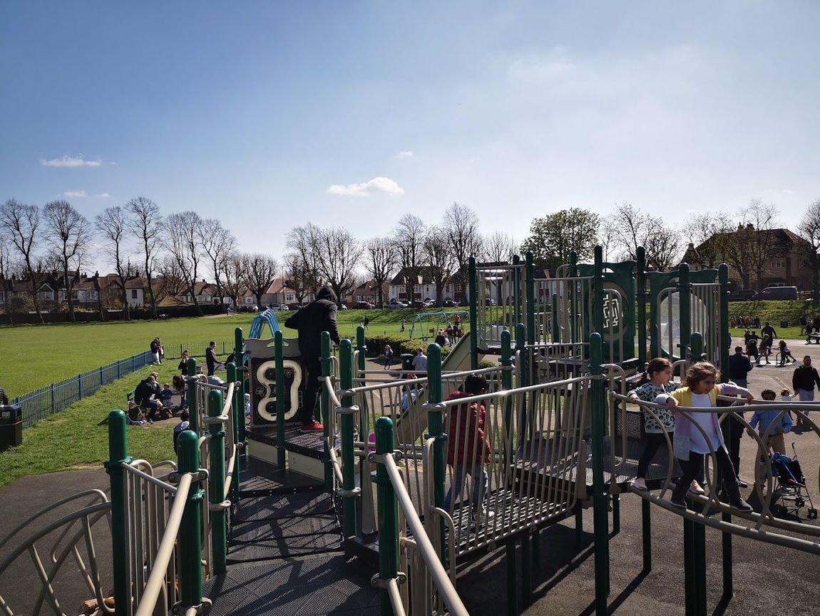 Children playing on a green playground with climbing structures in a sunny park