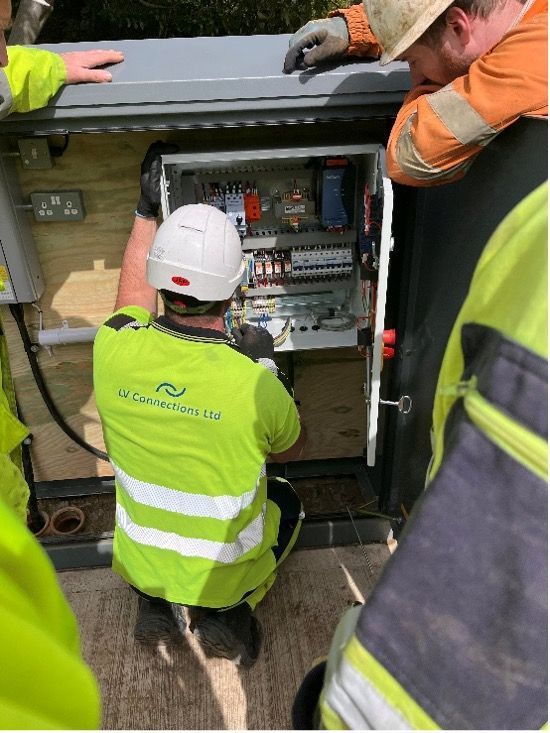 Workers inspect electrical panels inside an open roadside utility cabinet