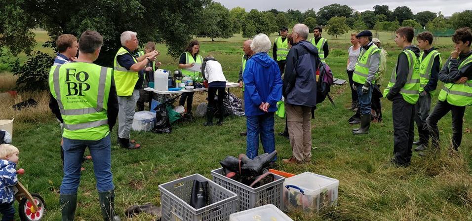 People in high-visibility vests gather outdoors near crates and tables in a grassy field.