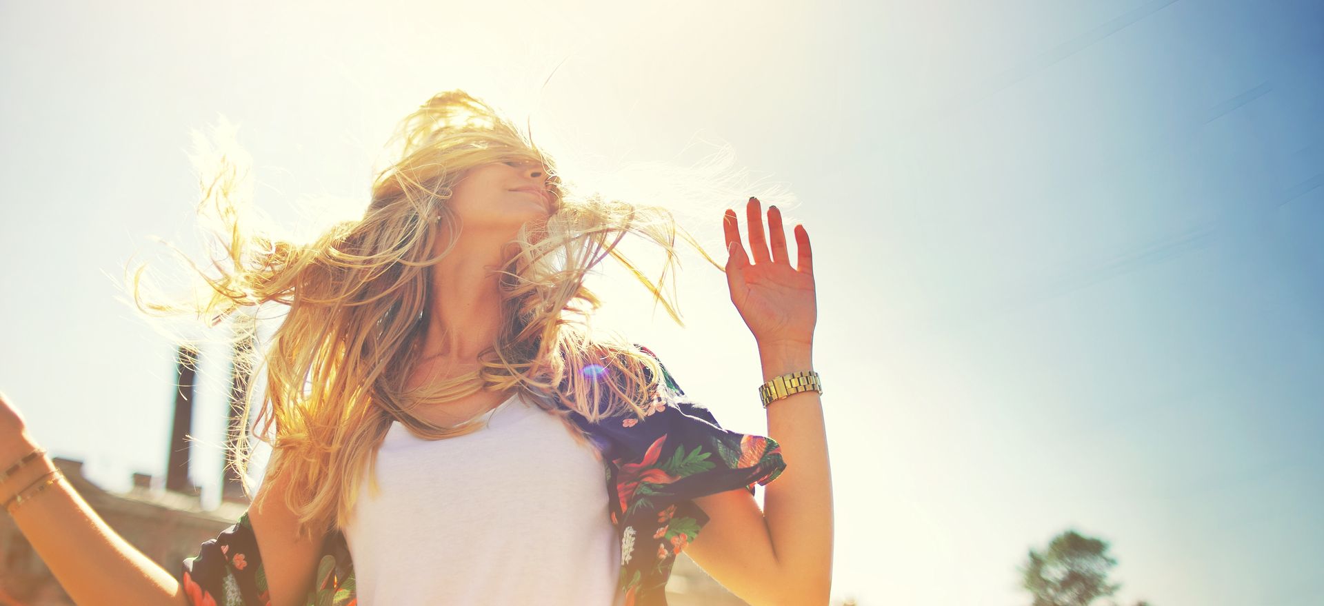 A woman is dancing in the sun with her hands in the air.