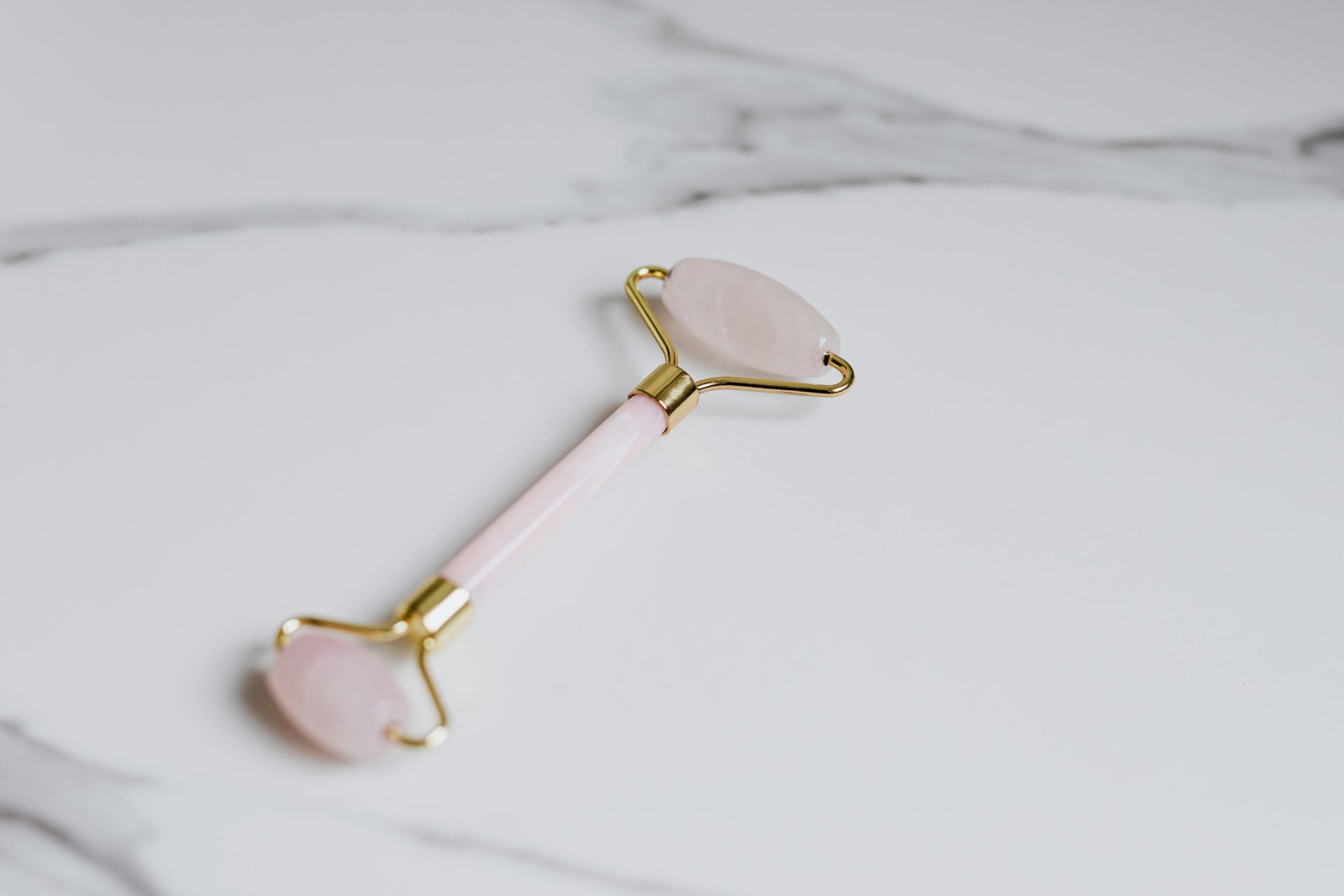 Pink jade face roller on a white marble surface.