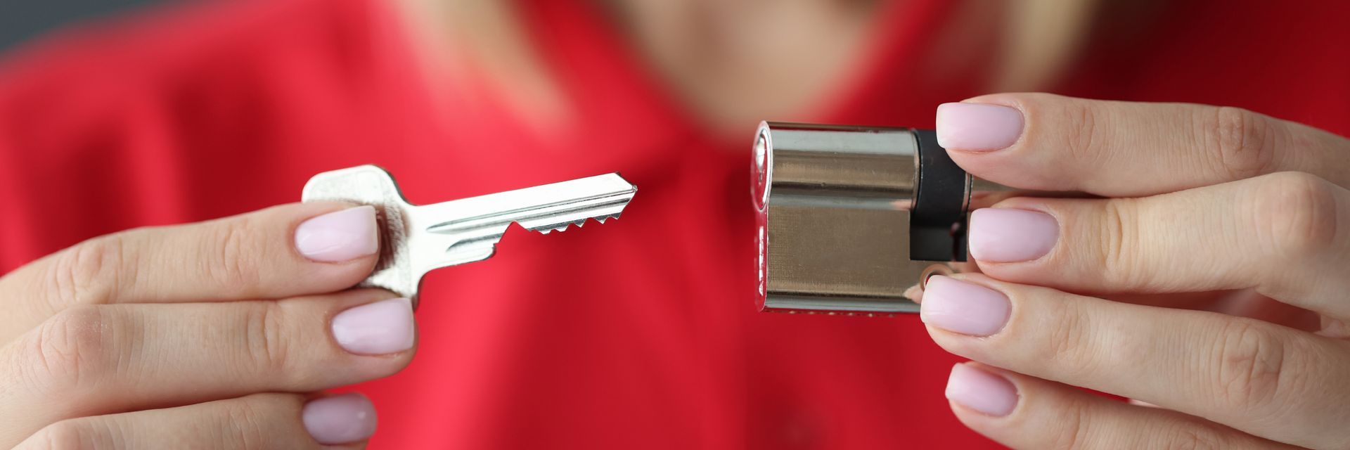 A person holding a key and a door lock cylinder; red shirt background.