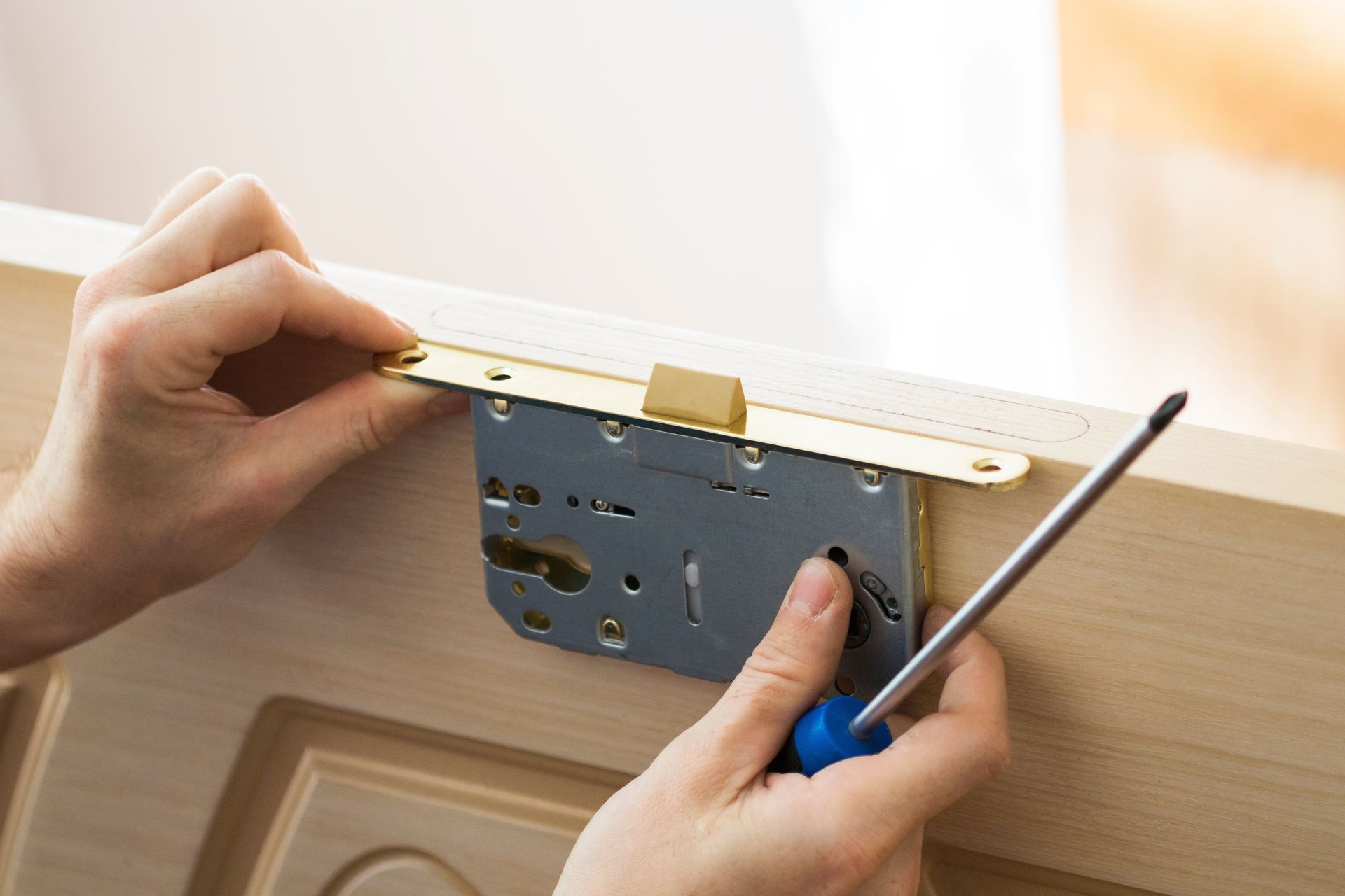 Person using a screwdriver to install a lock on a wooden door.