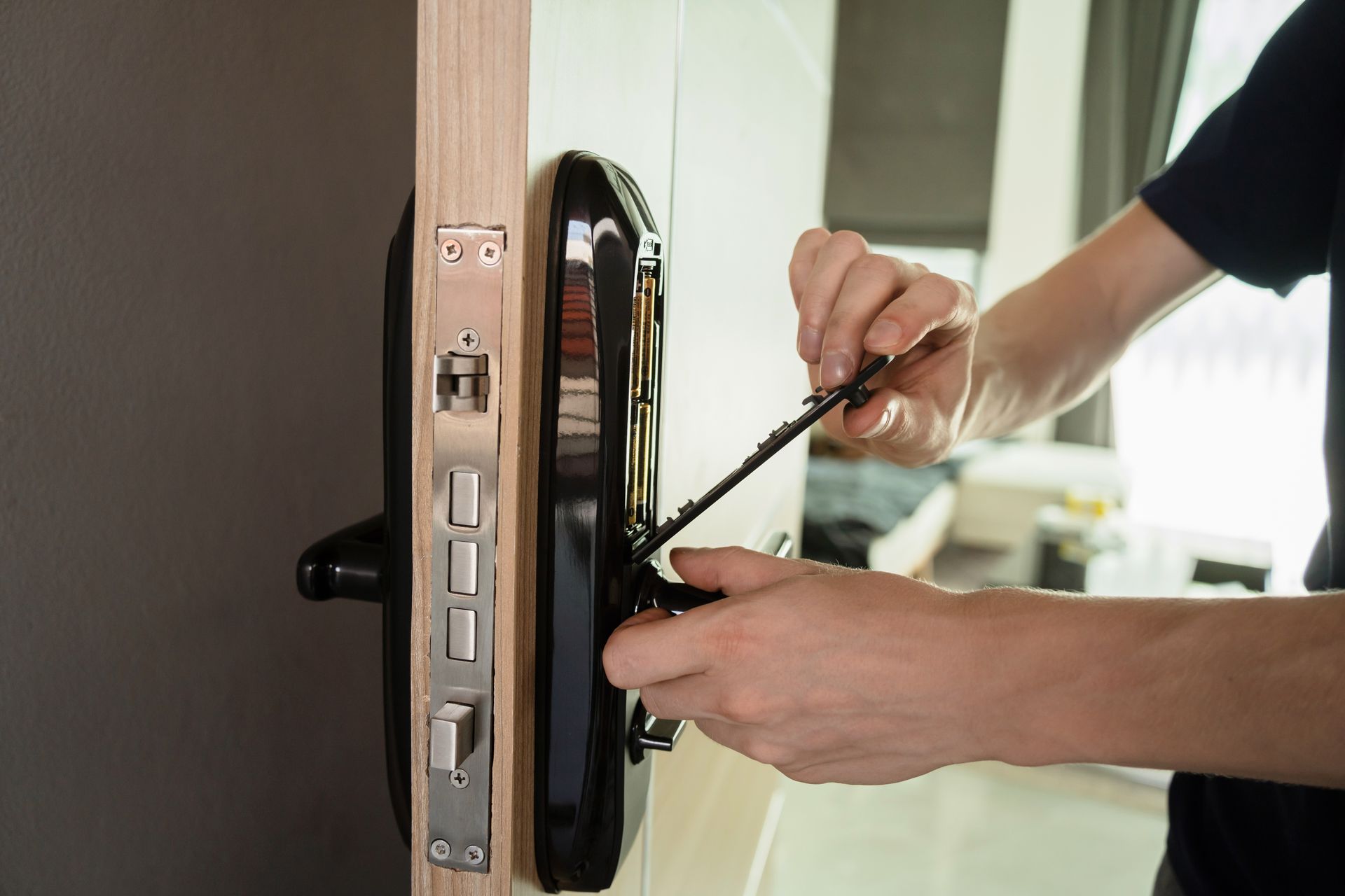 Person installing a black smart lock on a white door; interior setting.