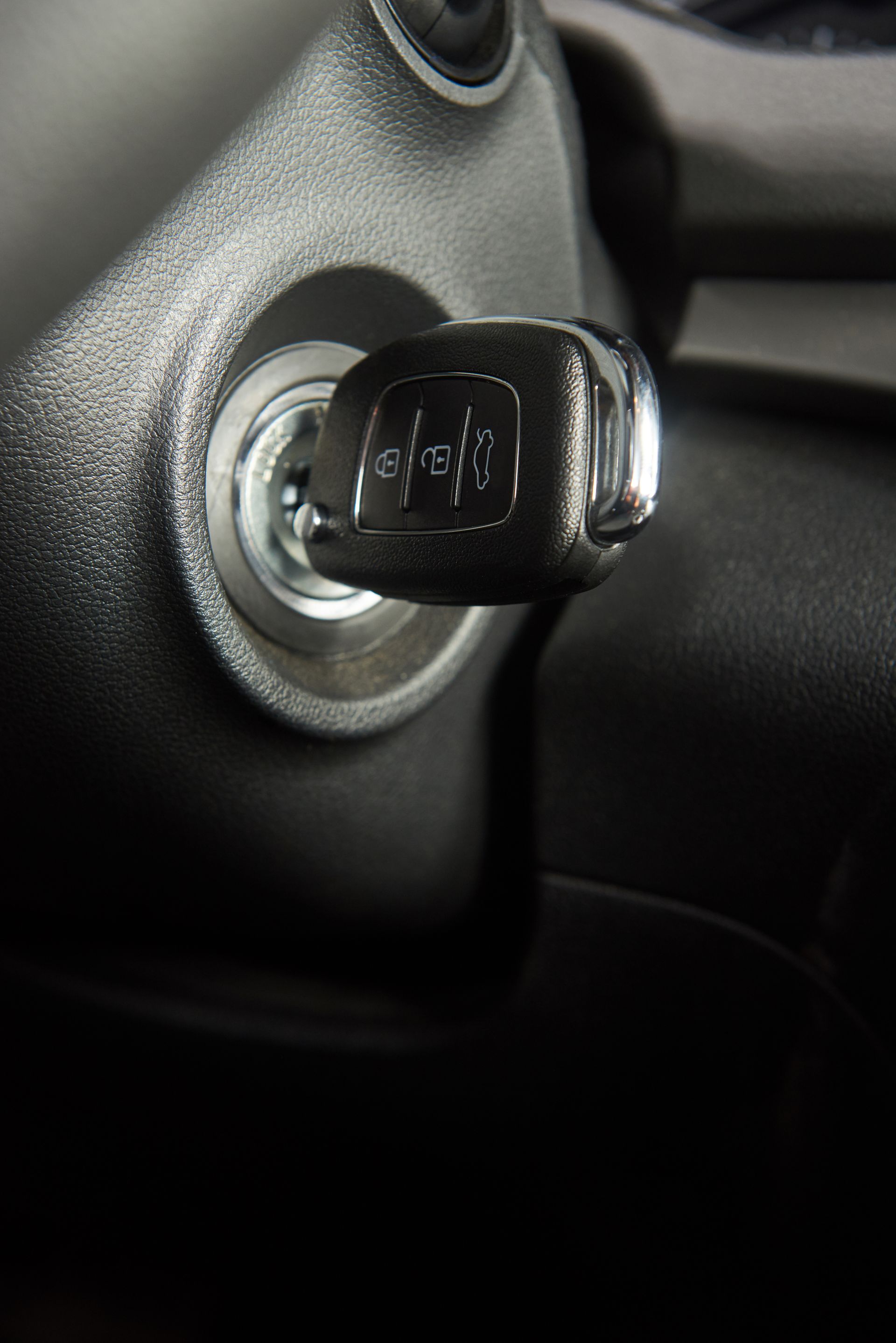 Car key in ignition, chrome key, black dashboard.