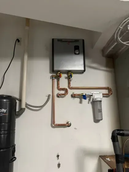 Wall-mounted water heater with copper pipes and a filter in a utility room