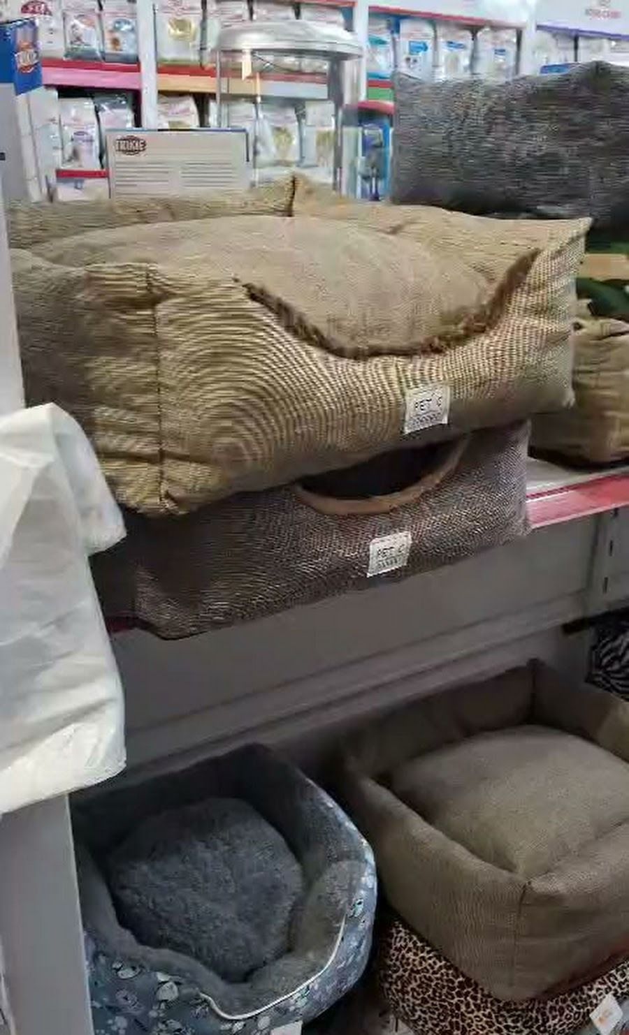 Camas para mascotas apiladas en los estantes de la tienda, incluyendo camas acolchadas de color beige, gris y azul.