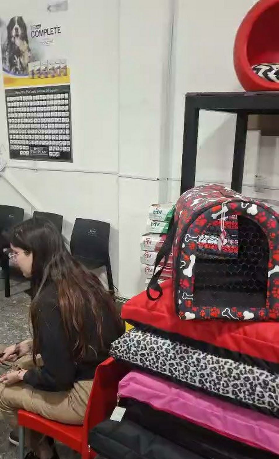 Persona sentada junto a un estante con mochilas rojas, negras y con estampado de leopardo en una tienda.