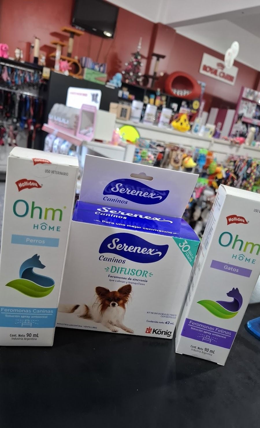 Tres cajas de productos para mascotas sobre el mostrador de una tienda, con el interior rosa del local al fondo.