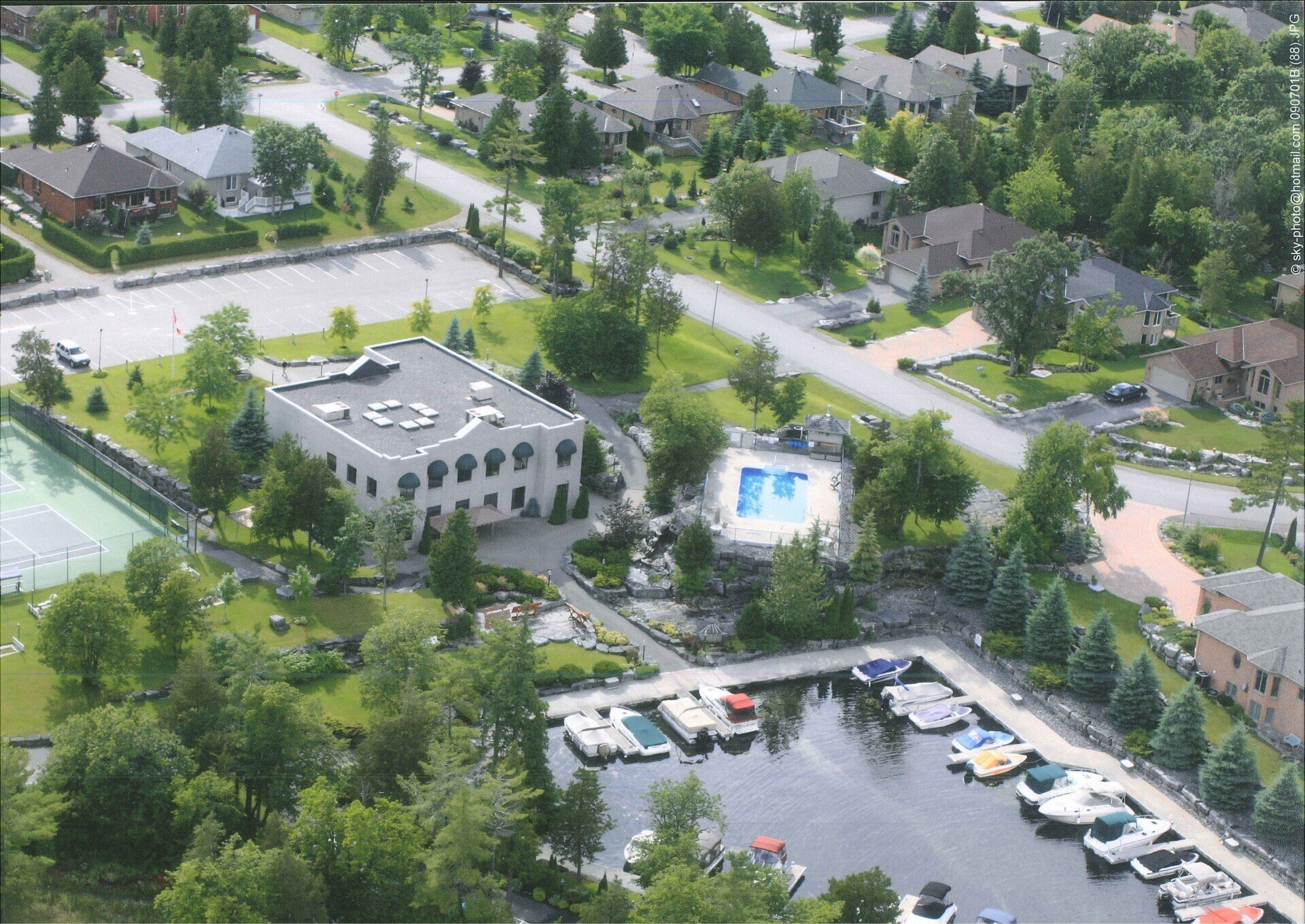 Aerial view of Port 32 marina with boats, a pool, Shore Spa, and houses. Green trees and grass surround.