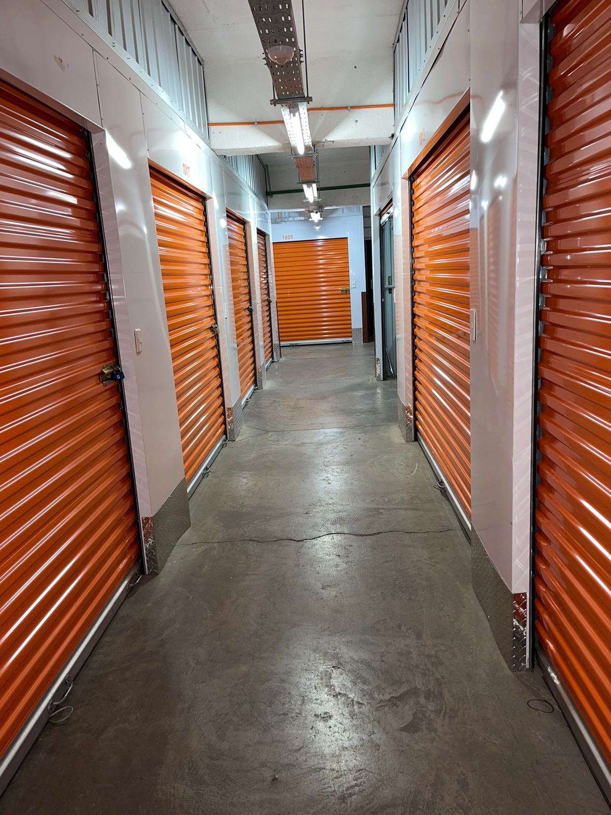 Filas de cajas de cartón apiladas sobre palés en un pasillo de un almacén con estanterías naranjas.
