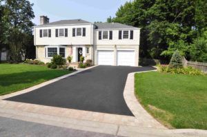 A two-story house with a white exterior, a stone foundation, and a newly paved asphalt driveway bordered by light pavers.