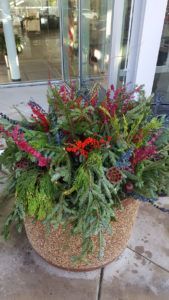 A large, textured tan planter filled with a lush arrangement of green ferns and vibrant red and purple flowering plants.