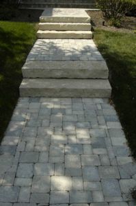 A stone walkway with two wide, elevated stone steps leading to a landing with a set of three additional concrete steps.