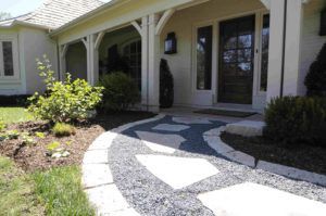 A walkway made of light-colored flagstones set in dark gray gravel leads to the front entrance of a house.