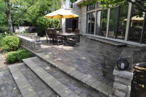 A stone patio with a table and yellow umbrella, featuring stepped levels and low stone walls with lanterns.