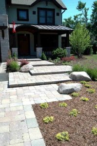 Stone paver walkway leading to the front porch of a house with stone steps, boulders, and mulched landscaping.