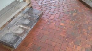 A set of gray stone steps leading to a red brick patio with a herringbone pattern.