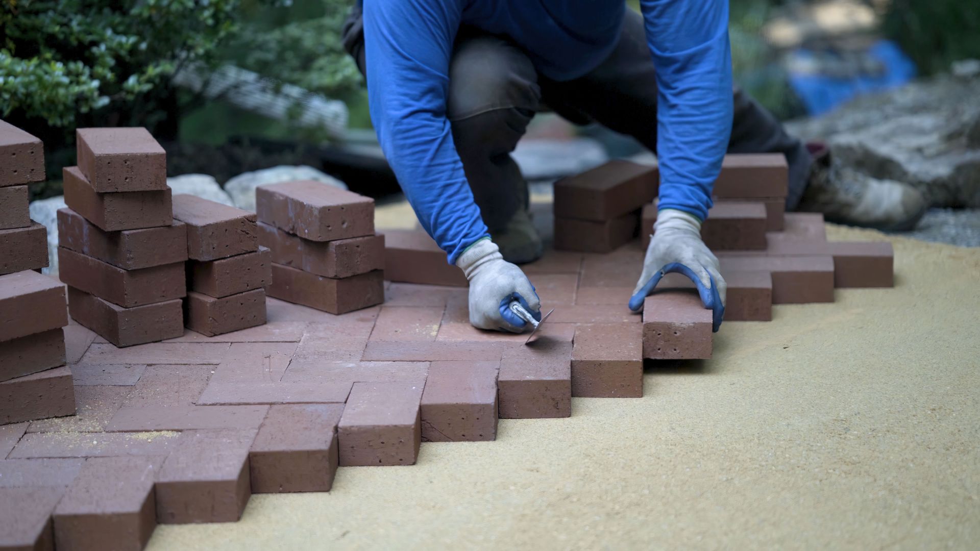 A hardscaper taps the red brick pavers into place on a bed. A hardscaper taps the red brick pavers into place on a bed.
