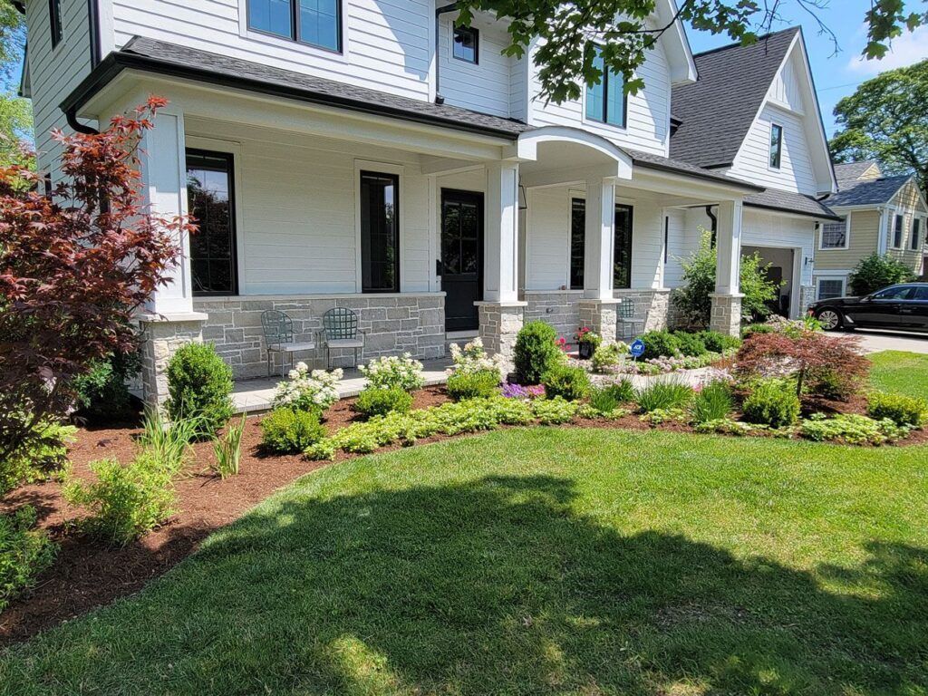 A two-story white house with a stone base, a covered front porch, and manicured landscaping in the front yard.