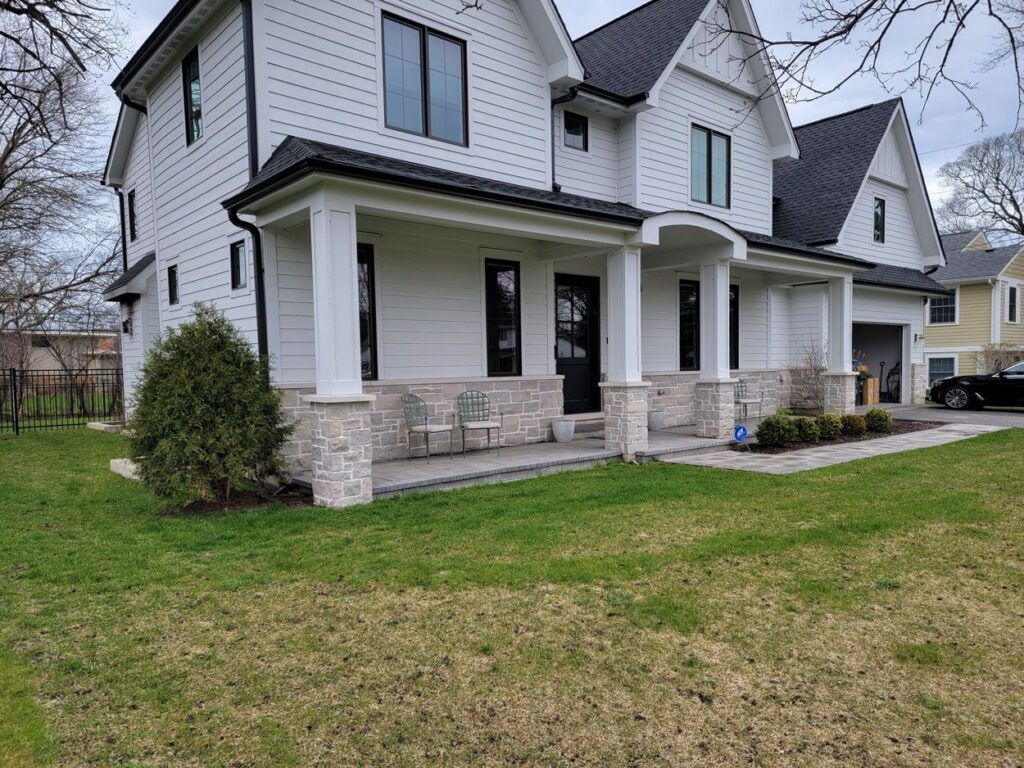 A modern two-story white house with black trim and a stone-based front porch, set on a grassy lawn.