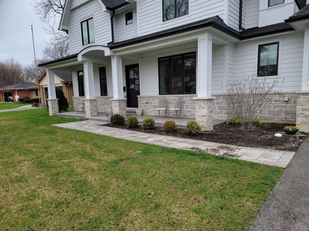 A white two-story house with a stone-accented porch, a gray stone walkway, and a landscaped front yard.