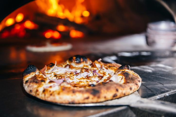 Una pizza viene tolta dal forno appoggiata su una pala.