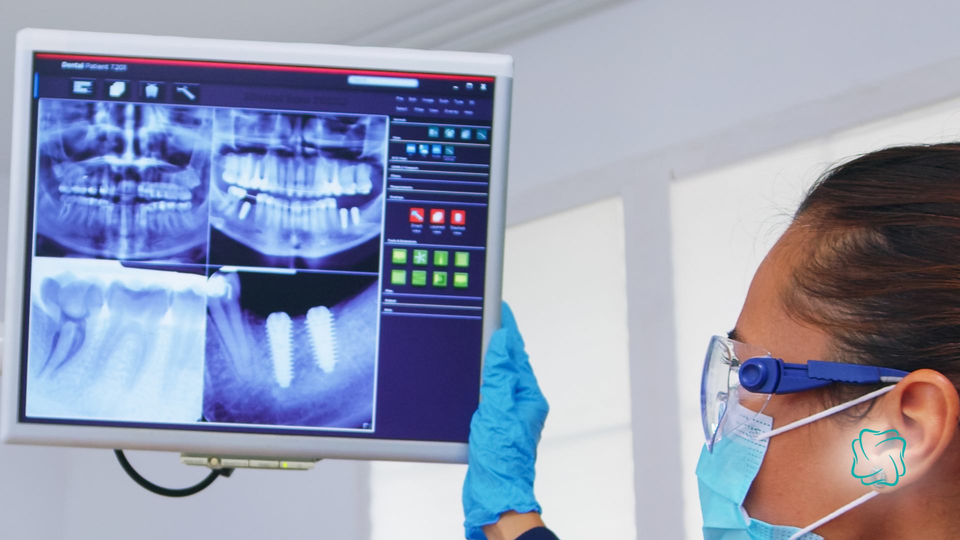 Dentist examining dental x-rays on a computer screen while wearing a mask, safety glasses, and gloves.
