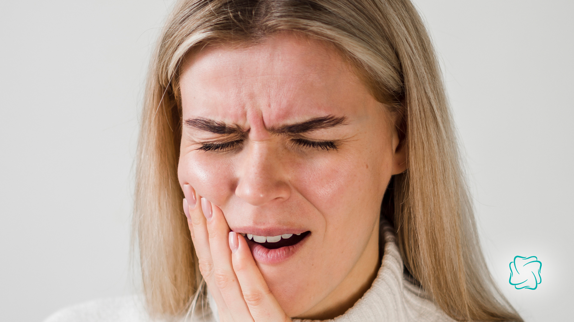 Woman with blonde hair, grimacing in pain, holding her jaw.