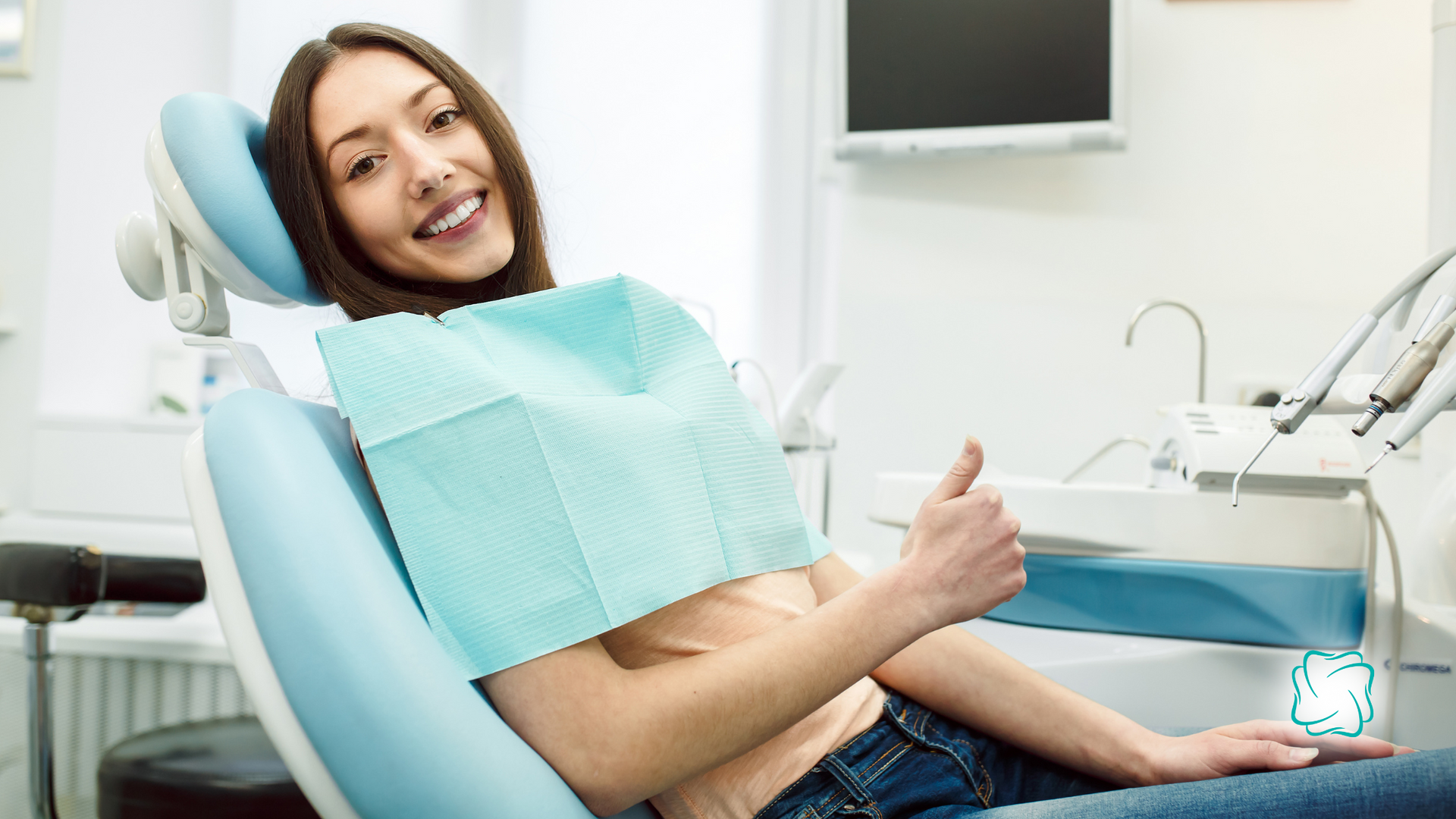 Woman in dentist chair gives a thumbs up, smiling, in a dental office.
