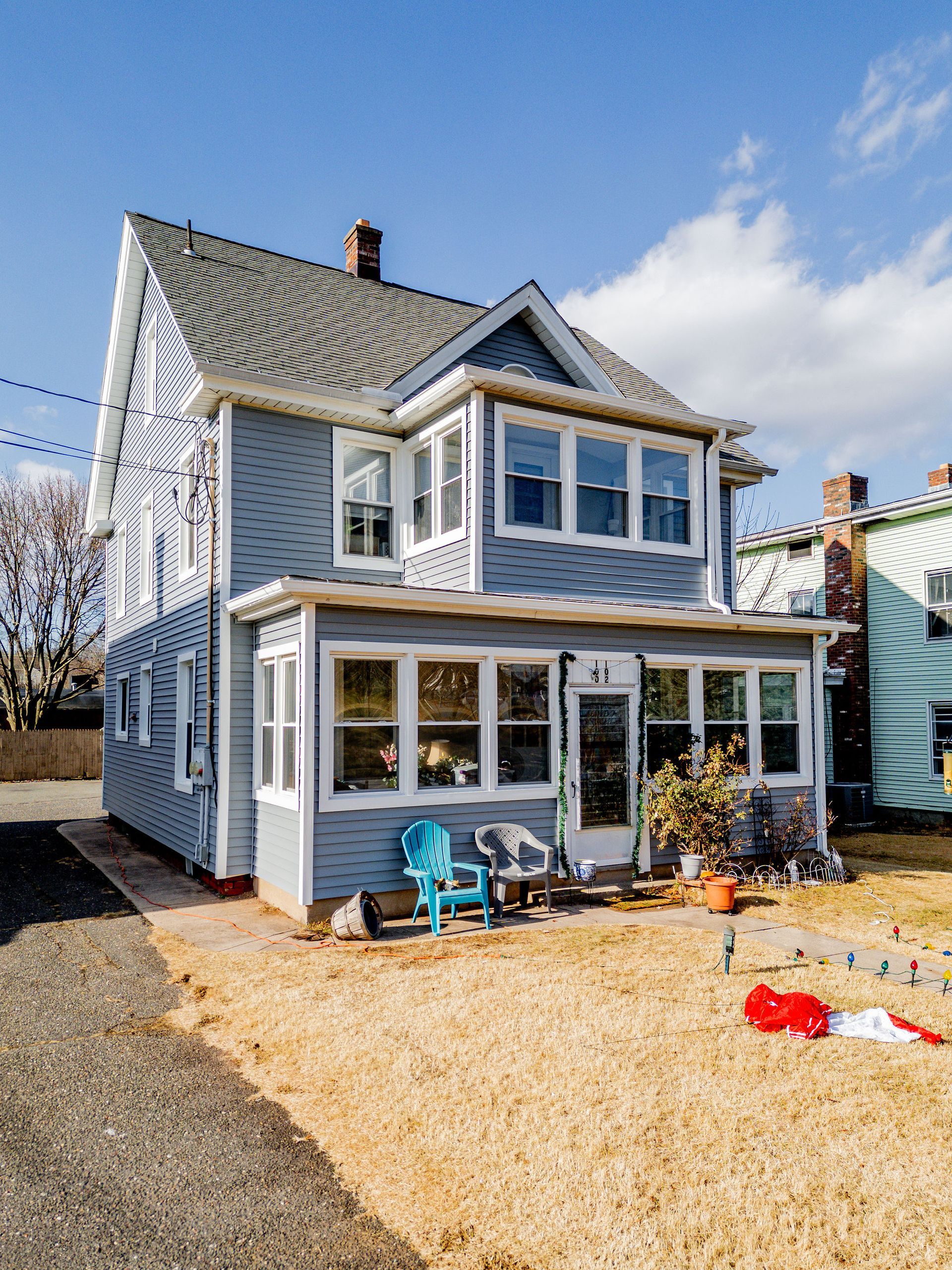 Two-story blue house with a sunroom, on a sunny day, with a brown yard.