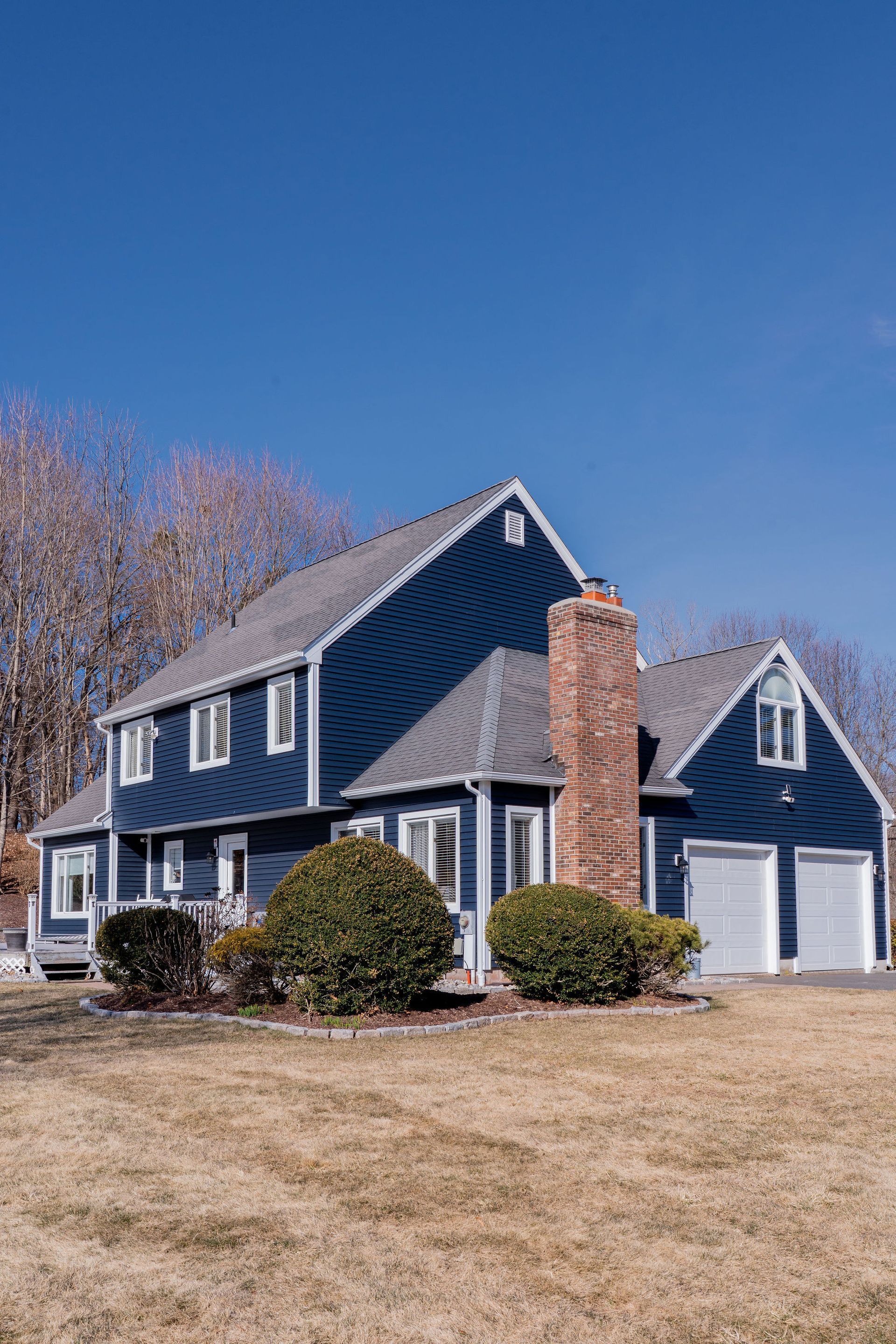 Blue house with white trim, brick chimney, and two-car garage under a bright blue sky.