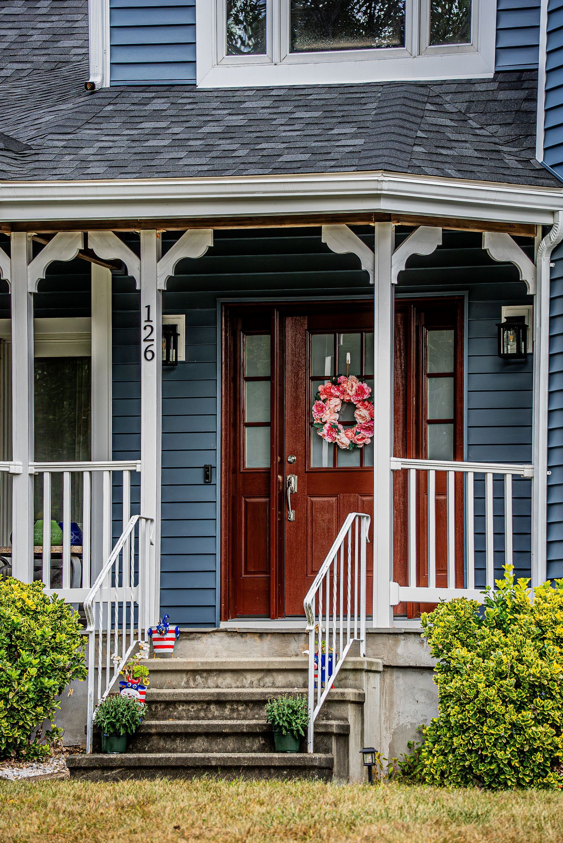 Front porch of a blue house with white trim, red door, wreath, and steps leading up to the entrance