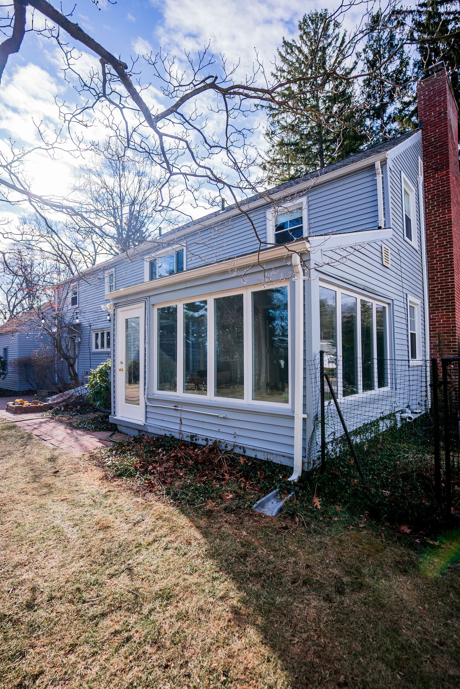 Two-story blue house with sunroom and brick chimney. Outdoors, sunlight, and dry grass.
