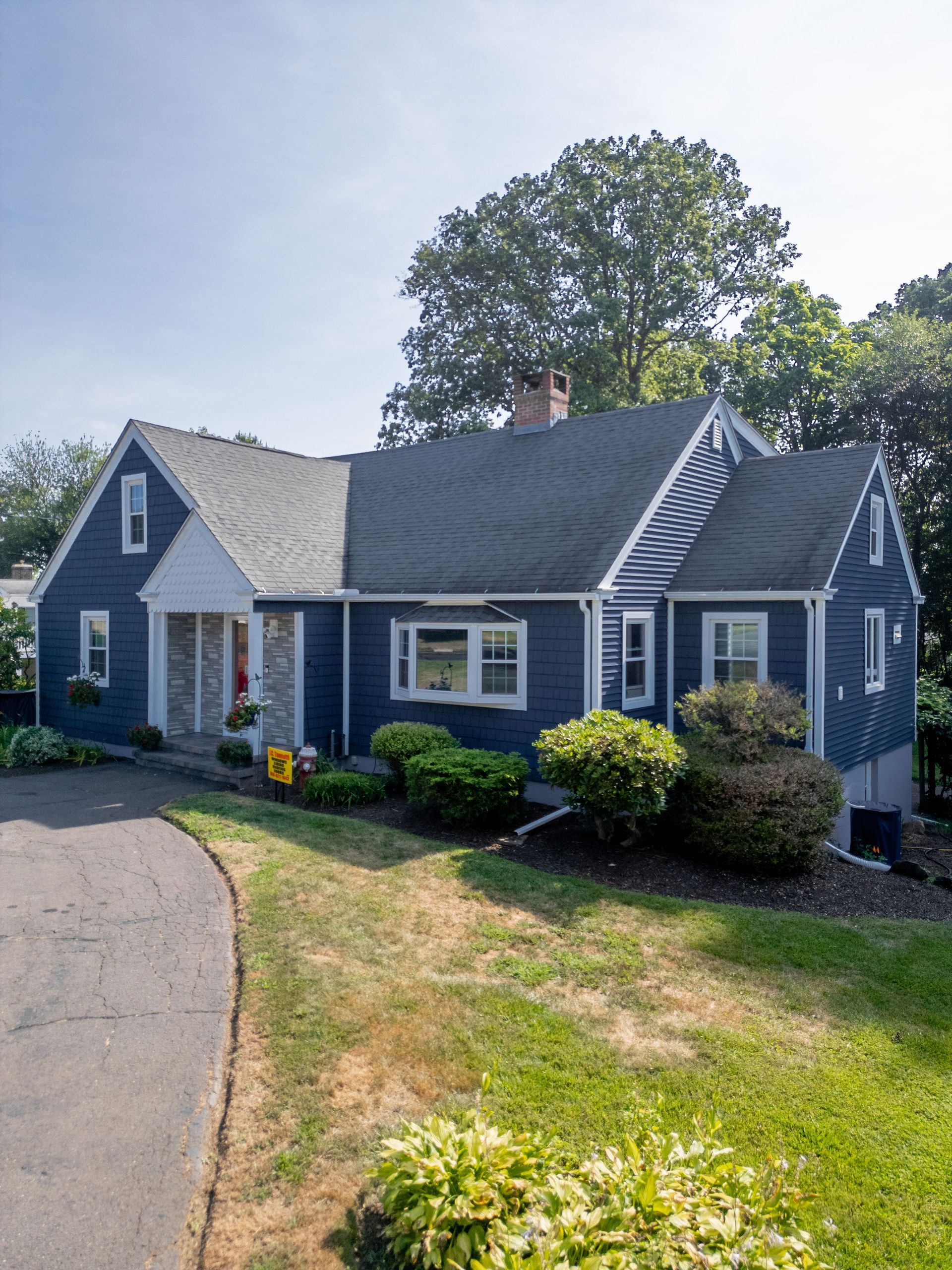 Blue house with white trim and a dark driveway on a sunny day.