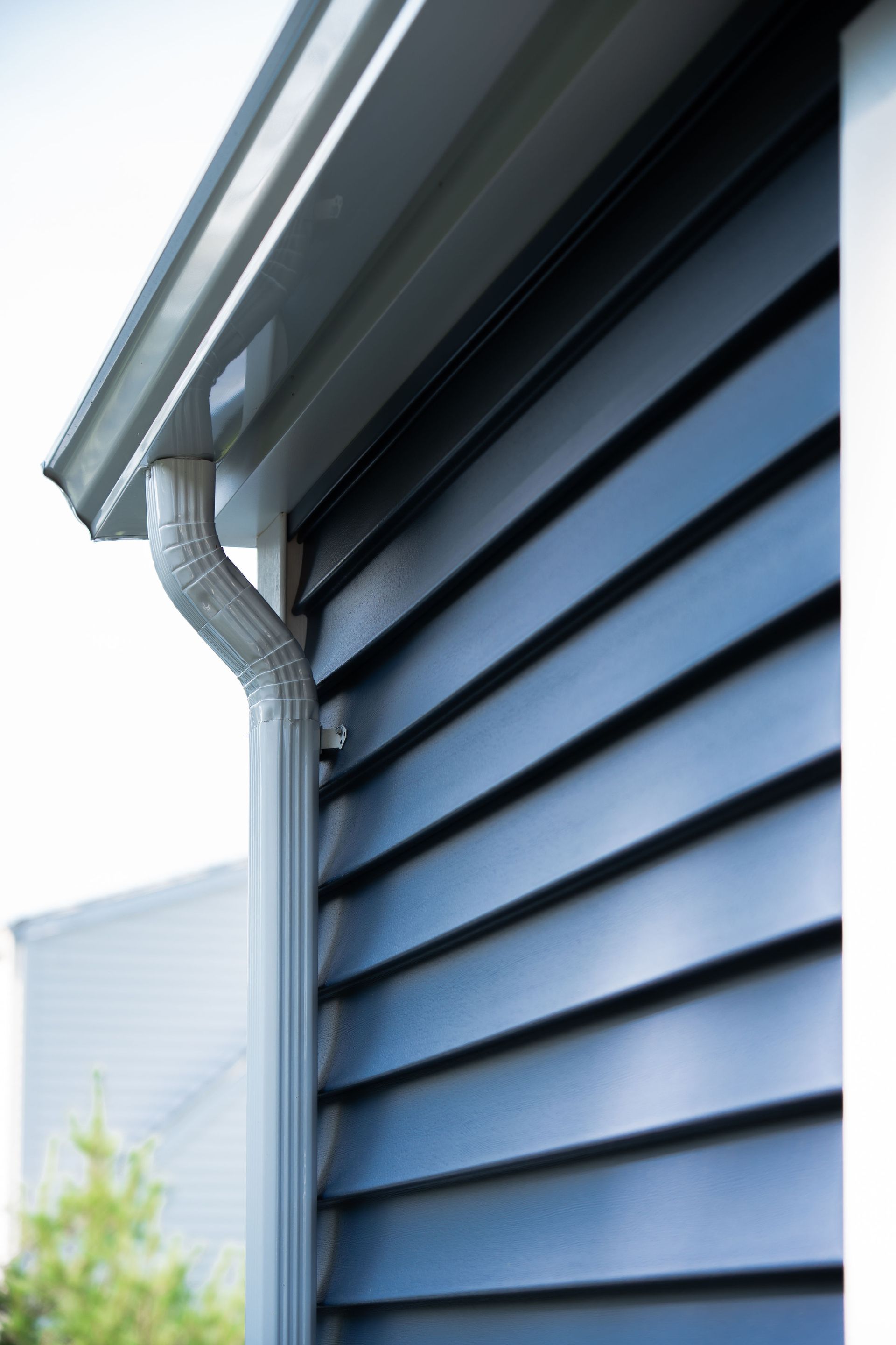 Dark blue siding with a gray gutter and downspout on a house.