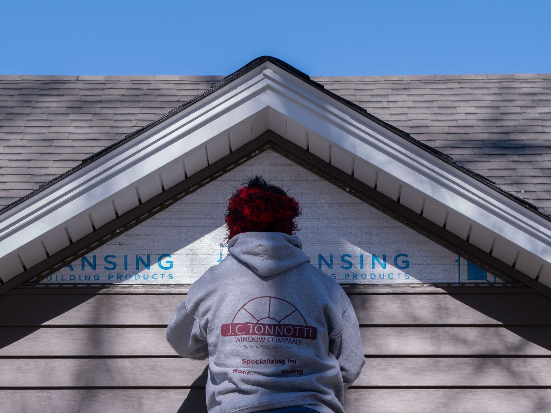 A man in a gray hoodie is working on a siding installation