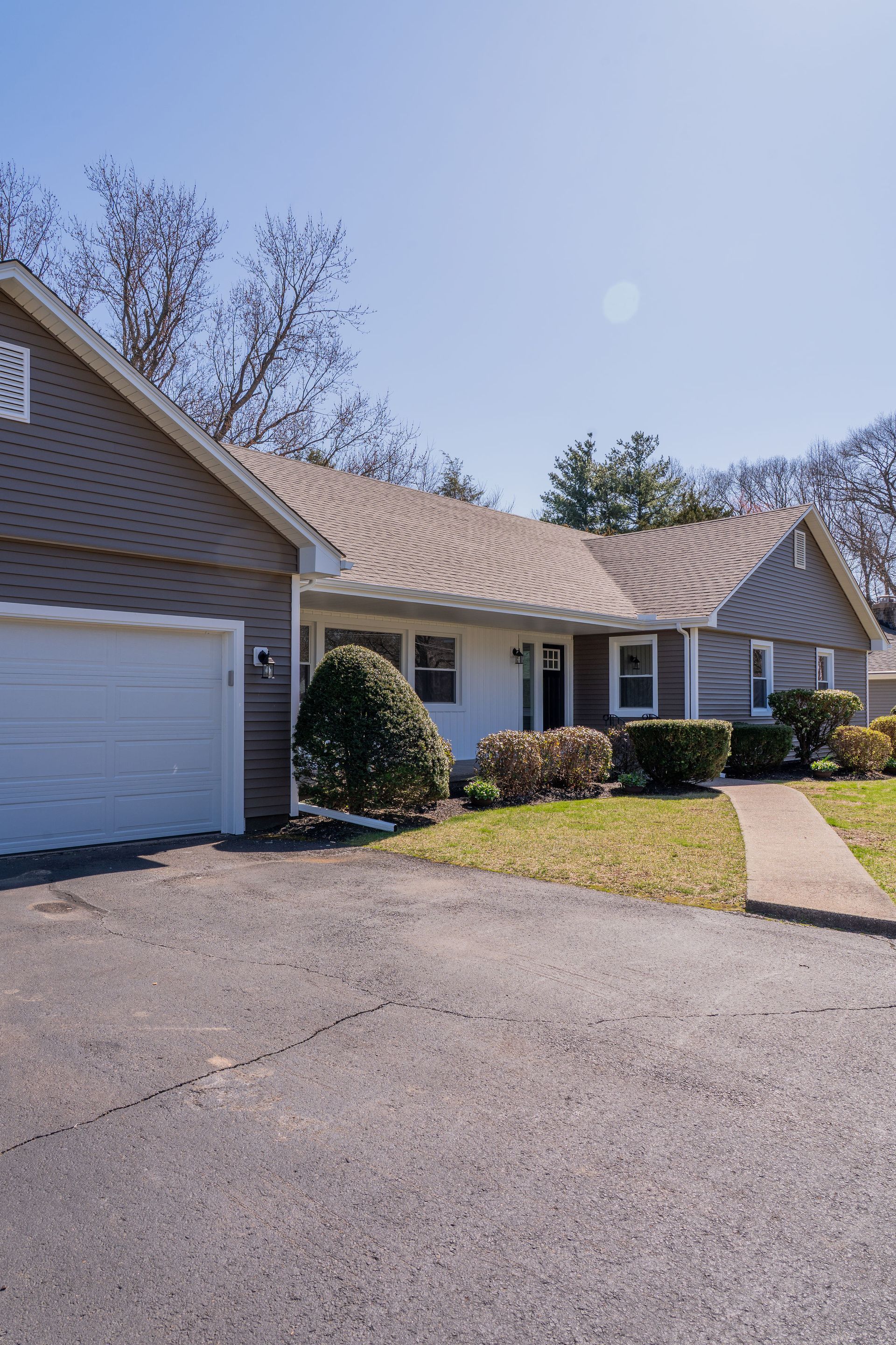 Ranch-style house with attached garage, light siding, asphalt driveway, and a clear blue sky.