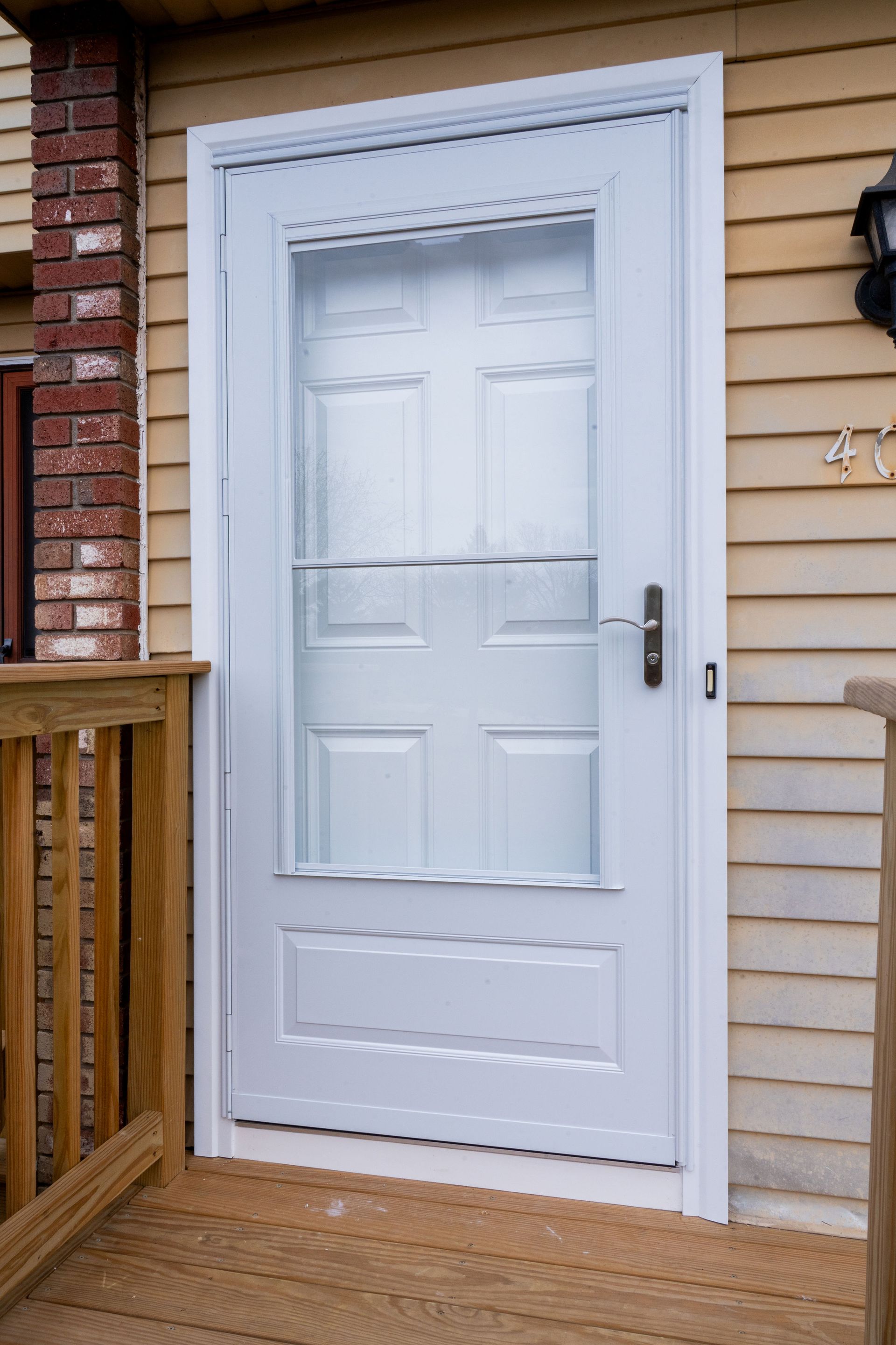 White screen door with glass panels, set in a wooden door frame. On a wooden deck next to a house.